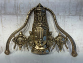 A detailed brass wall hanging depicting the face of Lord Venkateswara, adorned with a tall crown, traditional markings, and flanked by symbolic conch and discus motifs.